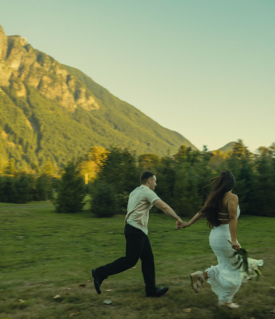 Bride and groom hold hands as they run away together after just eloping in front of Mount Si, one of the most gorgeous mountains. 