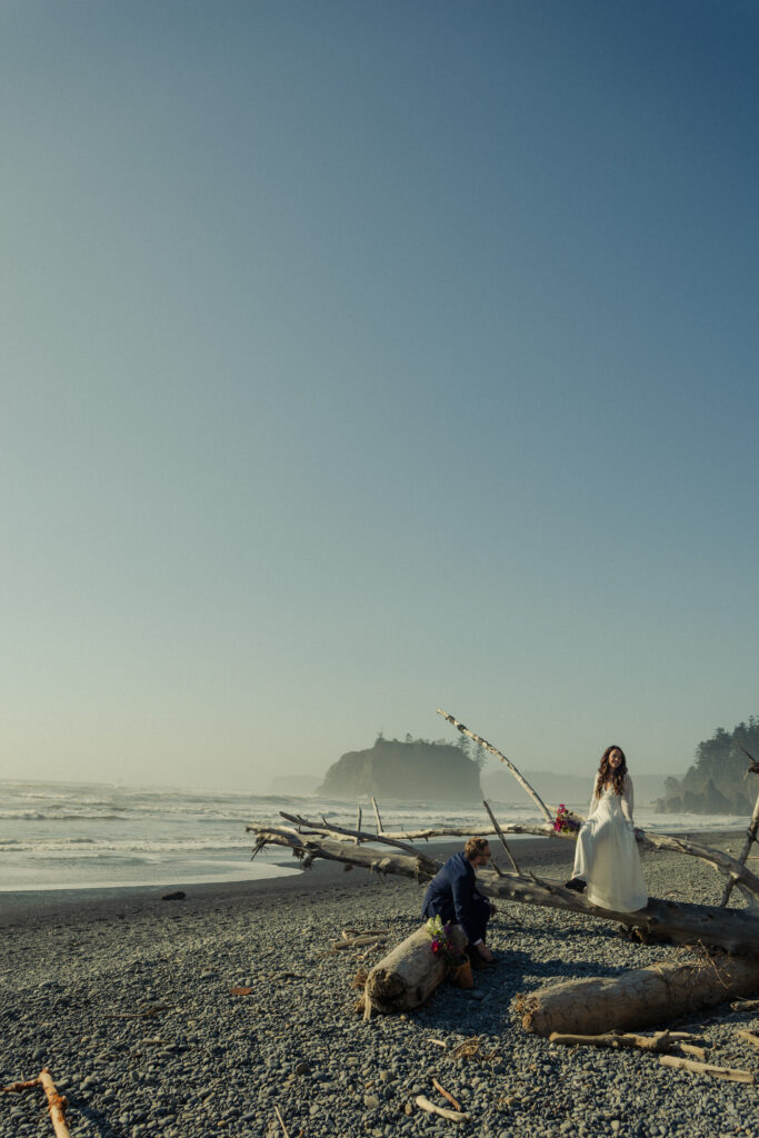 Bride and groom are sitting on the beach in Olympic national Park as they watch the waves crash and enjoy the peaceful day on the beach