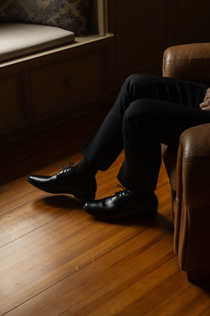 groom slips on his shoes as the final step of his getting ready process