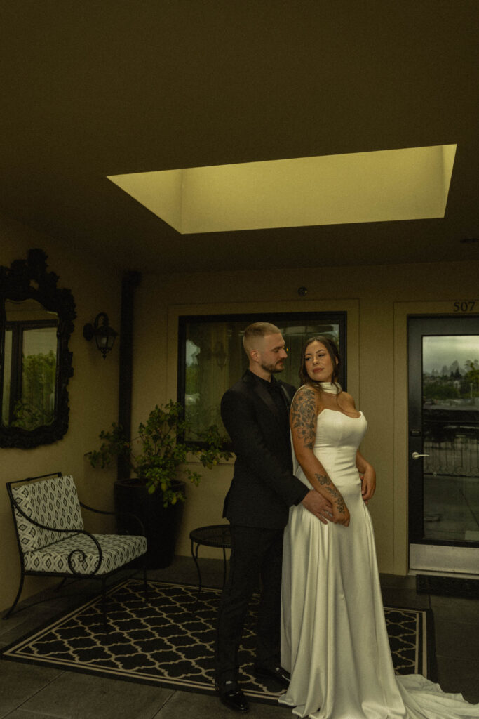 bride and groom cuddle close together. the groom has his hands around her waist as he looks down at her
